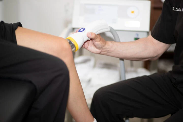 A medical practitioner applying Softwave Therapy to a patient's knee